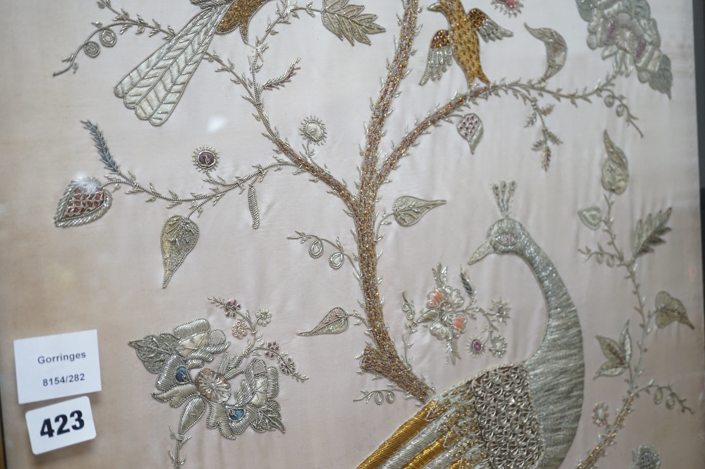 A framed silk, multi coloured metal thread embroidered Indian panel: a peacock seated amongst birds, flowers and leaves in a tree, 110cms x 51cms